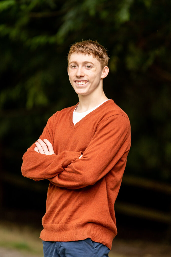 Ewan, a senior at Mountlake Terrace, standing confidently in his orange sweater at Carcreek Park for his senior photo session.