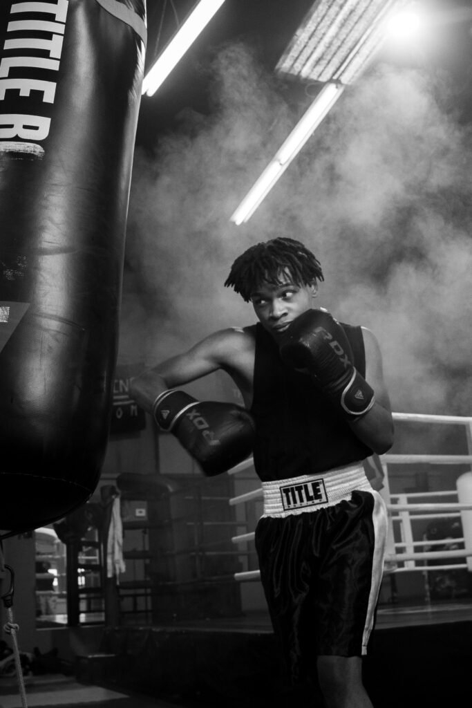 Josiah, a senior at Jackson High School, hitting a punching bag while the photographer captures the moment, with added smoke effects in black and white.